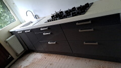 Moderne keuken zwart met wit werkblad, met gasfornuis, inbouwvaatwasser en -oven. - Foto 1